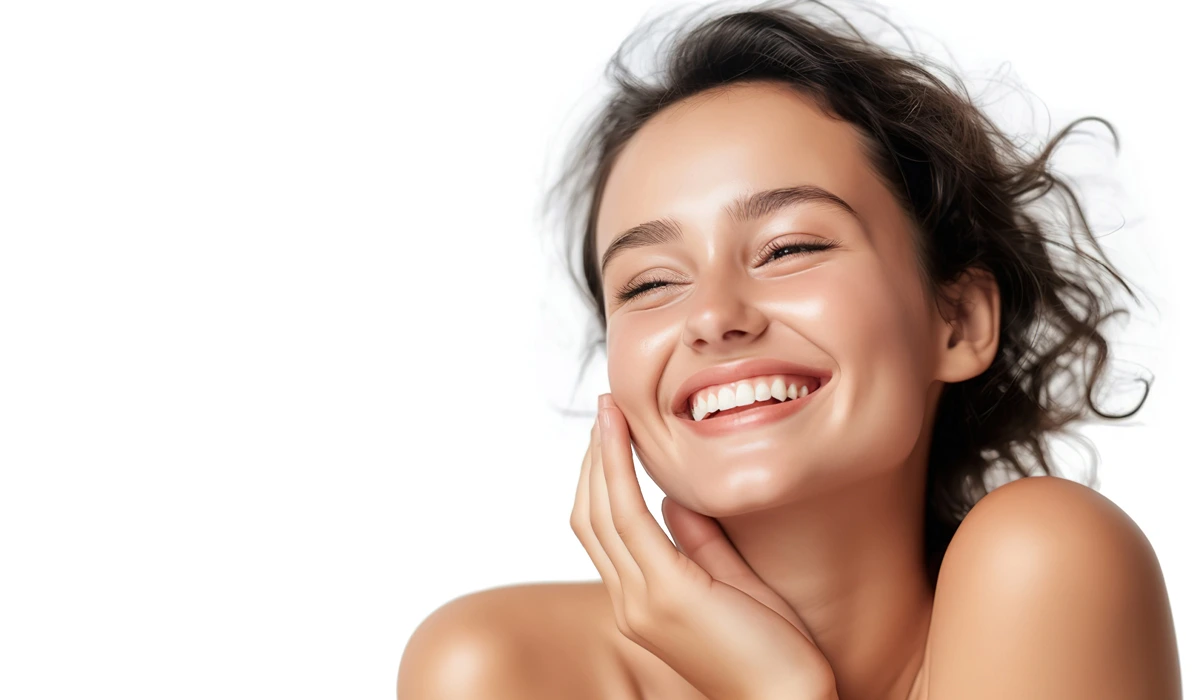 Woman smiling with hands on her face, showing radiant skin, surrounded by skincare products like cleansers and treatments