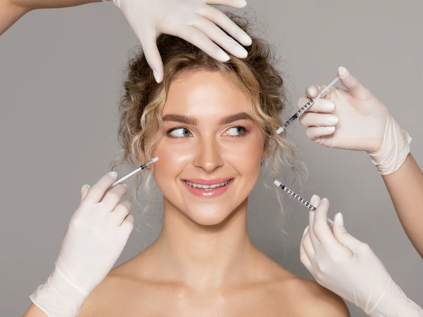 Multi Point Facial Injectable Treatment Concept A smiling young woman surrounded by several pairs of hands in white medical gloves holding syringes