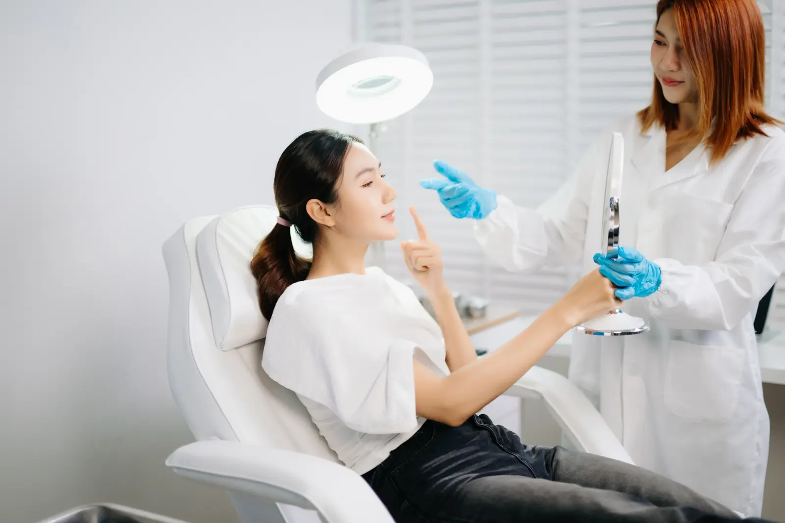 Patient consulting with aesthetician holding mirror in modern medspa office.